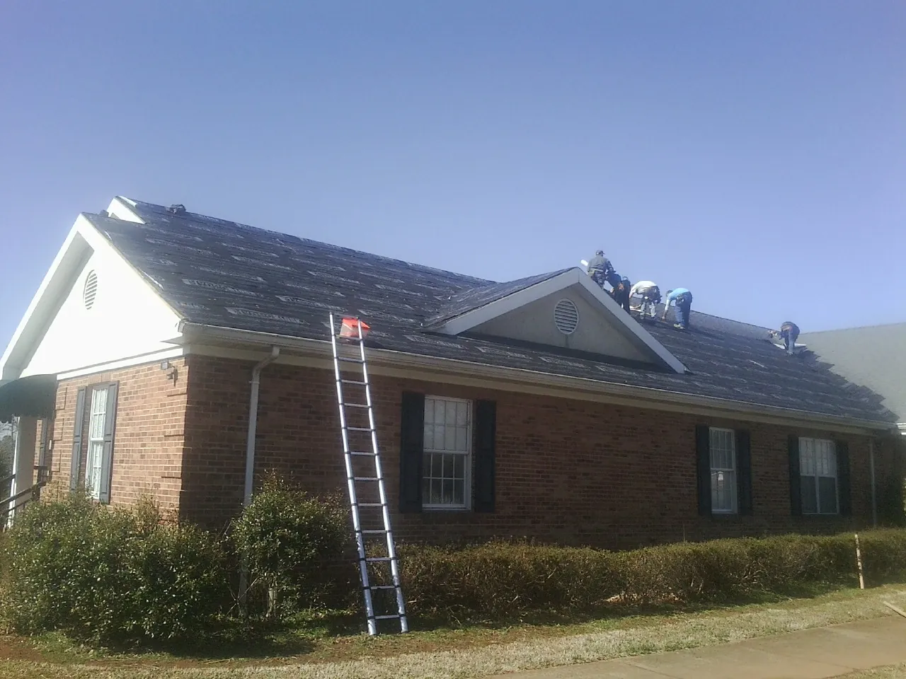 Crew tearing shingles off a brick ranch roof with a ladder set — Emergency Roof Repair work by our crew in Lilly