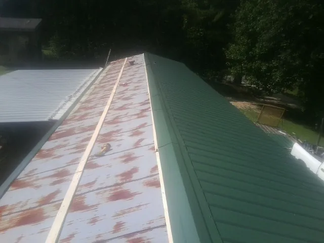 Old rusted panels beside newly installed green metal roofing — Wind Damage Roof Repair by Roofing Brothers in Lilly