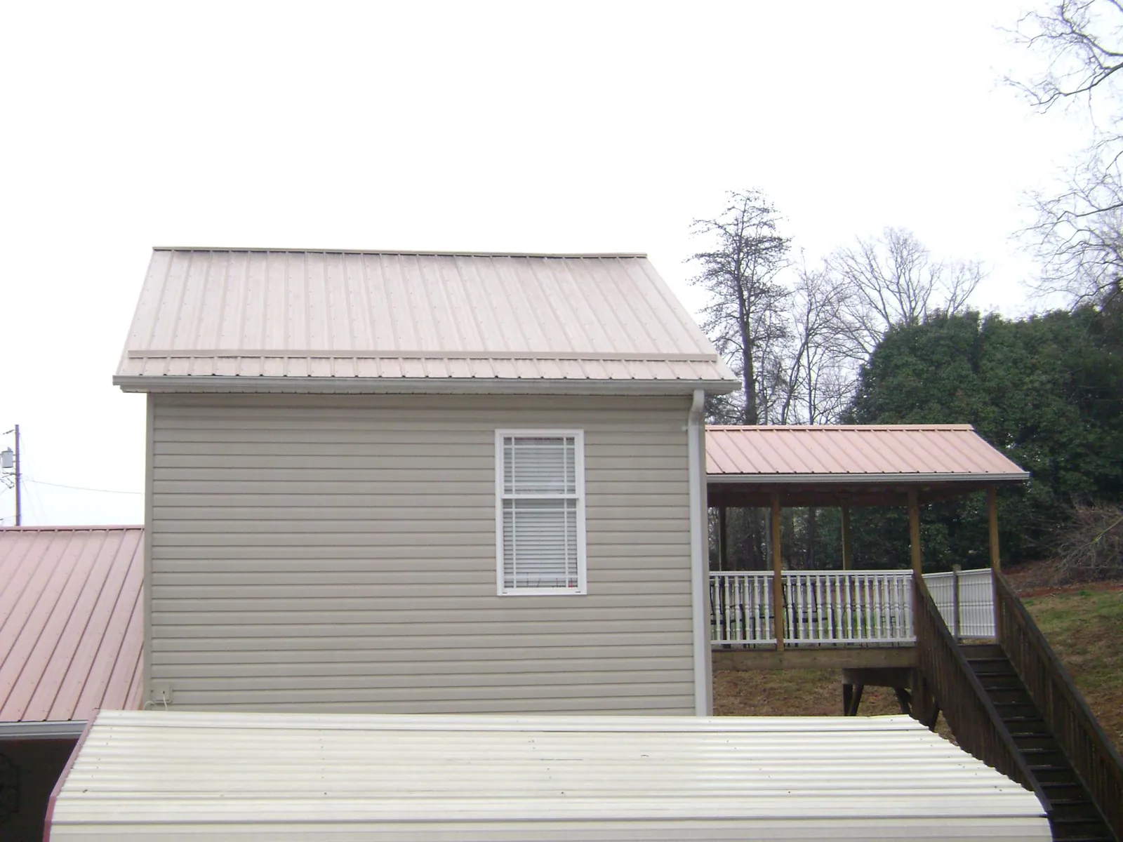 Tan metal roofs on a two story addition and attached porch, from a Roof Replacement job in Lilly